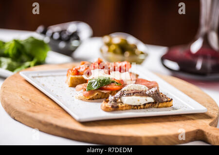 Gustoso antipasto italiano bruschettes con pomodori acciughe Prosciutto e mozzarella. Foto Stock