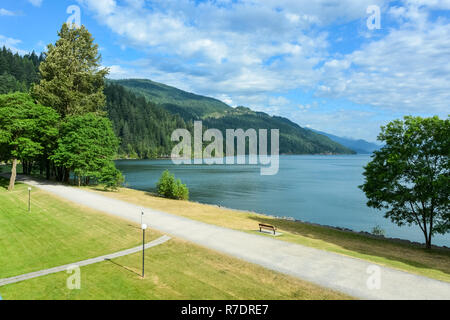 Vista sul lago di Harrison e le montagne con la passeggiata lungo la riva di fronte Foto Stock