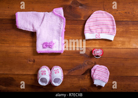 Baby vestiti e accessori in legno marrone tabella di sfondo, rosa bambino neonato Abbigliamento moda impostato per la ragazza, moderno bambino neonato bimbo abbigliamento kni Foto Stock