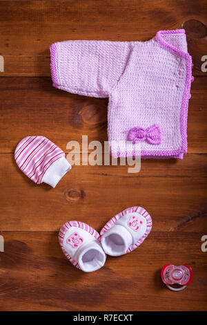 Vestiti del bambino in maglia rosa Maglione cotone guanti calzini e Falso su sfondo di legno, panno per neonati sul tavolo, bambino neonato Abbigliamento moda per g Foto Stock