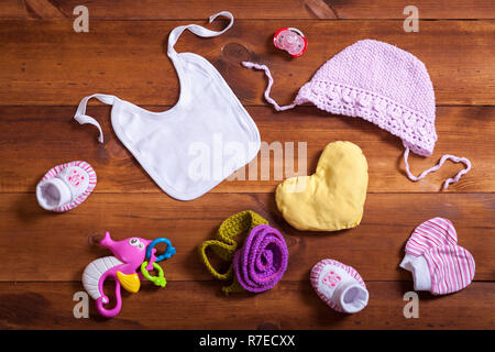 Vestiti del bambino set accessori, rosa cotone lavorato a maglia abbigliamento, giocattoli e kid bib sul legno marrone sfondo, bambino neonato panno di moda per la ragazza, moderno Foto Stock