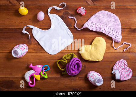 Vestiti del bambino set accessori, rosa cotone lavorato a maglia abbigliamento, giocattoli e kid bib sul legno marrone sfondo, bambino neonato panno per ragazza moderna in regalo Foto Stock