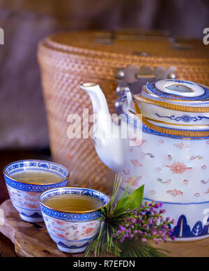 La porcellana cinese del tè pentola con il suo cesto di contenimento in background. Immagine di stock. Foto Stock