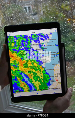 Donna mani tenendo ipad pro tablet allarme pioggia app utilizza in tempo reale radar a colori sovrapponendo i dati di pioggia sulla mappa locale di bagnato sulla finestra Essex REGNO UNITO Foto Stock