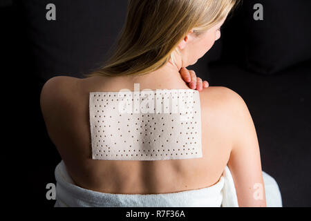 Giovane donna che soffre di dolori alla schiena ha applicato un intonaco di calore Foto Stock