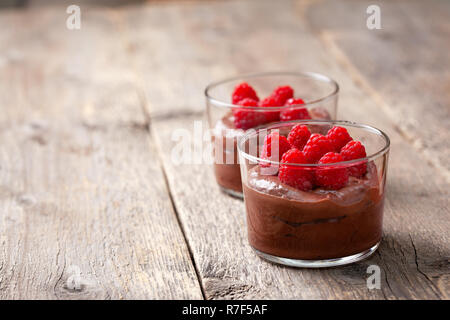 Mousse al cioccolato con lamponi in vetro bicchieri di servizio sul vecchio sfondo di legno Foto Stock
