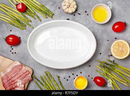 Ingredienti per cuocere gli asparagi con pancetta affumicata su un cemento grigio Sfondo. vista da sopra Foto Stock
