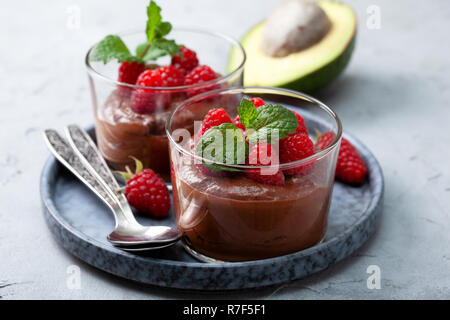 Avocado mousse al cioccolato con lamponi in vetro bicchieri di servizio su un sfondo grigio Foto Stock