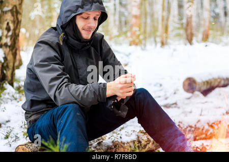 Giovane uomo si siede su un log in inverno Foto Stock