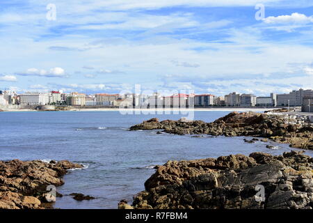 La Coruña, Galizia, Spagna. Vista da una passeggiata. I colori autunnali, bay, rocce, Spiaggia di Riazor e città. Mare blu, cielo nuvoloso. Foto Stock