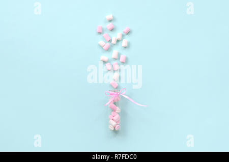 Rosa e Bianco marshmallow pezzi viene spruzzato da un piccolo contenitore di vetro su un pastello blu sullo sfondo. Piatto minimalismo laici. Vista superiore Foto Stock