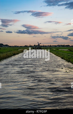 Onde in un canale olandese con una bellissima prospettiva. Un mulino a vento distante sorge alla fine del canal all'orizzonte. Foto Stock