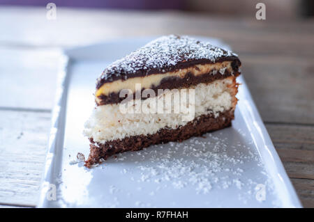 Torta al cocco sulla piastra bianca su tavola in legno rustico Foto Stock