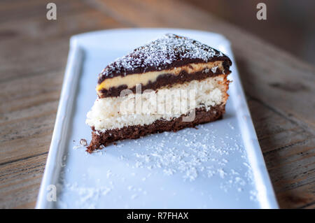 Torta al cocco sulla piastra bianca su tavola in legno rustico Foto Stock