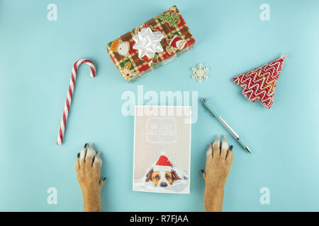 La scrittura di Natale greeting card concept, vista dall'alto. Zampe di cane, anno nuovo cartolina e vacanze puntelli su fondo azzurro Foto Stock