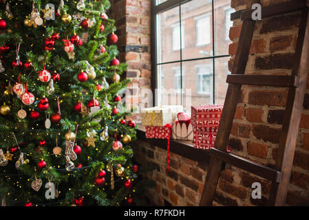 Albero di natale vicino alla finestra, sul davanzale dono e palloncini. scala di legno. anno nuovo 2019 Foto Stock