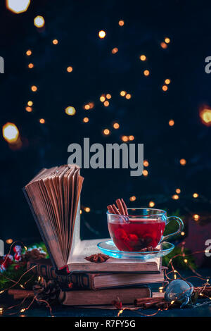 Bacca rossa tè su una pila di libri con le luci fairy. Drink di natale su sfondo scuro con spazio di copia Foto Stock