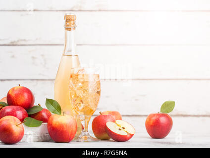 Bottiglia e bicchiere di organico in casa sidro di mele con mele fresche nella casella su sfondo in legno e vetro con cubetti di ghiaccio Foto Stock