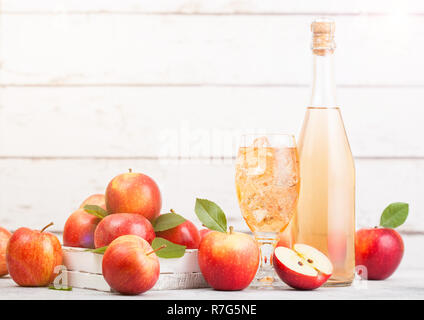 Bottiglia e bicchiere di organico in casa sidro di mele con mele fresche nella casella su sfondo in legno e vetro con cubetti di ghiaccio Foto Stock