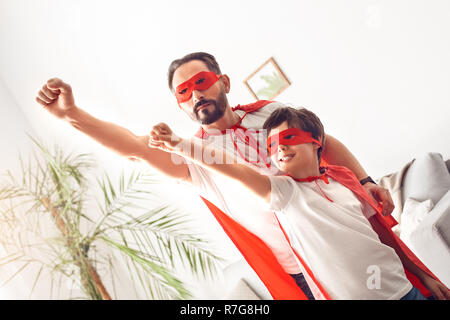 Padre e figlio in costumi superheroe a casa in piedi mani battenti eccitato Foto Stock