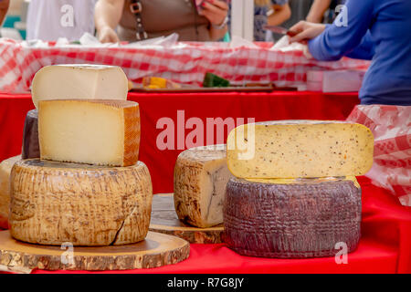 Impilate i turni di formaggio sono visualizzate in all'aperto il mercato degli agricoltori mentre la gente shop. Un formaggio server è consegnare campioni gratuiti di formaggio. Foto Stock