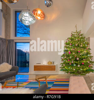 Contemporanea piano aperto spazio soggiorno in casa con altezza doppia windoes, Tom Dixon luci e albero di Natale. Foto Stock