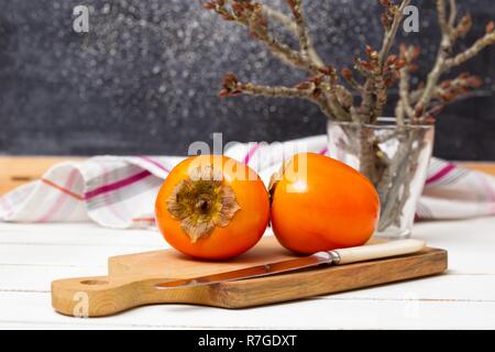 Cibo sano. Due cachi sono sul bordo, un coltello e un asciugamano Foto Stock