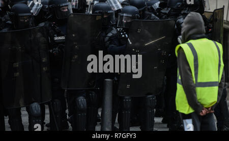 Parigi, Francia - 8 Dicembre 2018: Giallo canottiere (Gilets jaunes) protester sorge nella parte anteriore del francese riot ufficiali della polizia nel corso di una protesta contro livin Foto Stock