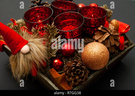 In prossimità della corona di Avvento con quattro candele, abete, palle di Natale, una nana e un cono di abete su sfondo nero Foto Stock
