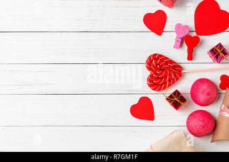 Il giorno di San Valentino decorazioni con lecca-lecca a forma di cuore, confezioni regalo e caramelle sul bianco sullo sfondo di legno con copia spazio, vista dall'alto Foto Stock