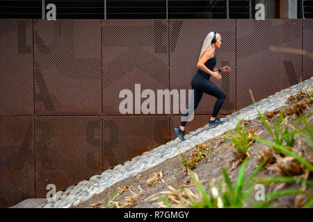 Montare le donne sportive esecuzione di allenamento a intervalli in scale contro una parete metallica in città Foto Stock