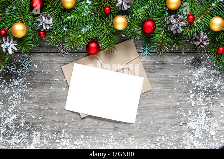 Auguri di Natale carta con abete rami e decorazioni su rustico sfondo di legno ricoperta di neve. mock up. laici piatta Foto Stock