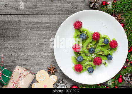 Kiwi albero di natale con abete rami e confezioni regalo su tavola in legno rustico. divertente idea di cibo per i bambini. Natale e Anno Nuovo sfondo alimentare. Foto Stock