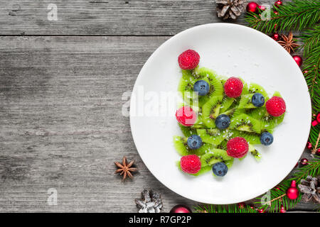 Kiwi albero di natale con abete rami su tavola in legno rustico. divertente idea di cibo per i bambini. Natale e Anno Nuovo sfondo alimentare. vista superiore Foto Stock