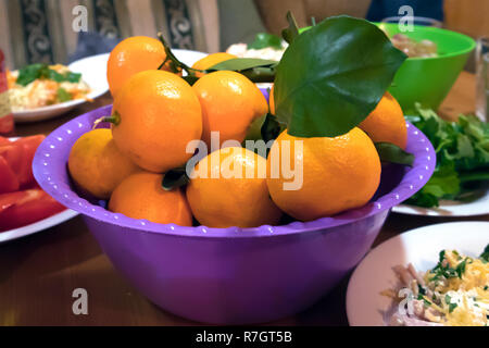 Succosa mature tangerini freschi con foglia verde in un viola coppa in plastica su un rustico tavolo di partito Foto Stock