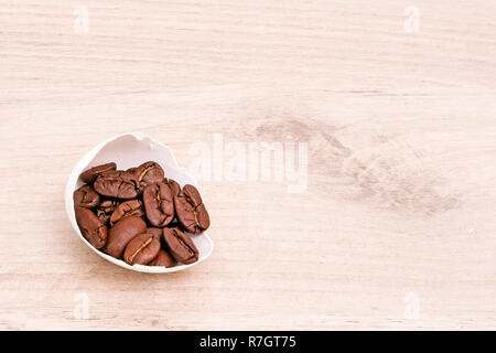 Una metà del bianco guscio d'uovo piena di caffè torrefatto in grani posto su una superficie in legno Foto Stock