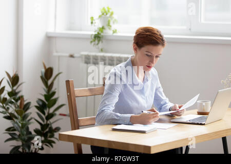 Focalizzato donna seduta alla scrivania del controllo dei dati nei documenti Foto Stock