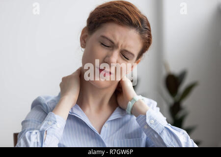 La donna soffre di dolori al collo mentre si lavora in ufficio Foto Stock