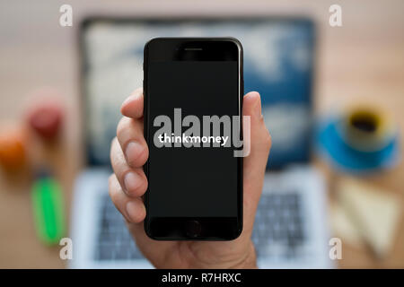 Un uomo guarda al suo iPhone che visualizza il logo ThinkMoney (solo uso editoriale). Foto Stock