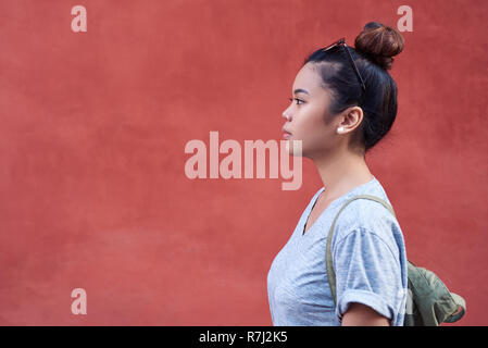Giovane donna asiatica lateralmente in piedi di fronte a una parete Foto Stock