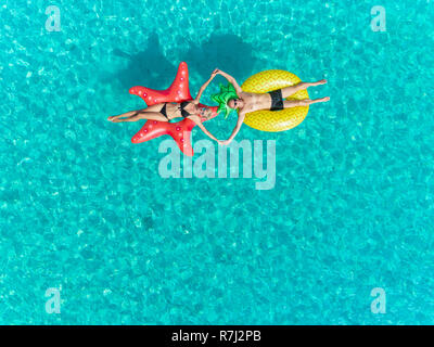 Antenna vicino la vista di un uomo e di una donna sul galleggiante gonfiabile di star e ananas materassi sagomati tenendo le mani. Foto Stock