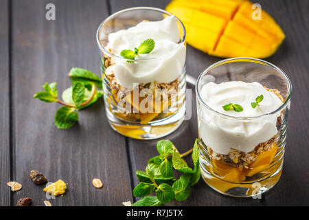 Lo yogurt greco mango parfait di muesli in un vetro su legno scuro dello sfondo. Foto Stock