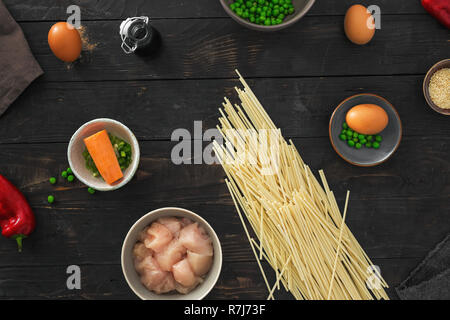 Materie prime per la cottura di udon tagliatelle con carne di pollo su legno scuro tabella vista superiore Foto Stock