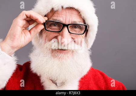 Ritratto di Babbo Natale con la barba bianca che indossano occhiali e Santa vestito in piedi su uno sfondo grigio, Anno nuovo, Natale, vacanze, souvenir e regali, shopping, sconti, negozi Foto Stock