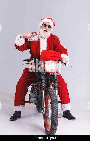 Babbo Natale con la barba bianca che indossa gli occhiali da sole e Santa outfit seduto sul motociclo e tenendo un sacco di soldi, Anno nuovo, Natale, vacanze, souvenir e regali, shopping, sconti, negozi, Snow Maiden Babbo Natale,make-up, Hairstyle, carnevale. Foto Stock