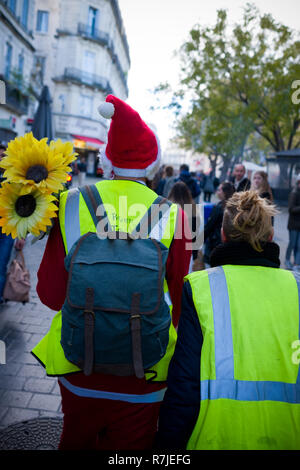 Vista posteriore di un francese di uomo e di una donna con il loro "gilets jaunes' e santa hat a camminare su high street nel centro di Montpellier, Francia Foto Stock