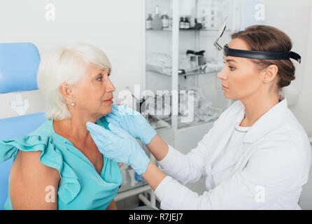 Il medico ORL esaminando gola della donna senior presso la clinica Foto Stock