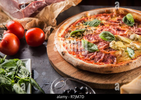 Pizza Quatro stagioni four seasons tradizionale pasto italiano di carciofi Funghi pomodori prosciutto formaggio parmigiano e basilico. Foto Stock