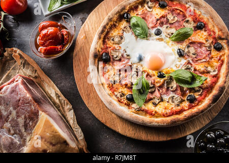 Pizza capricciosa capricciosa tradizionale pasto italiano dal prosciutto funghi carciofi uovo olive parmigiano e basilico. Foto Stock