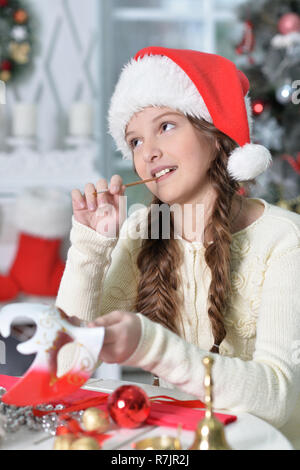 Felice ragazza in Santa hat la preparazione per il Natale seduti a Foto Stock